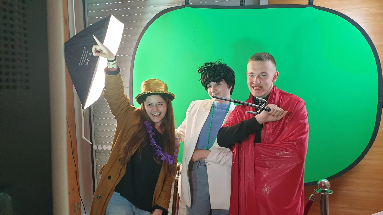 Trois invités déguisés (chapeau doré, cape rouge) posent devant le fond vert éclairé par un softbox