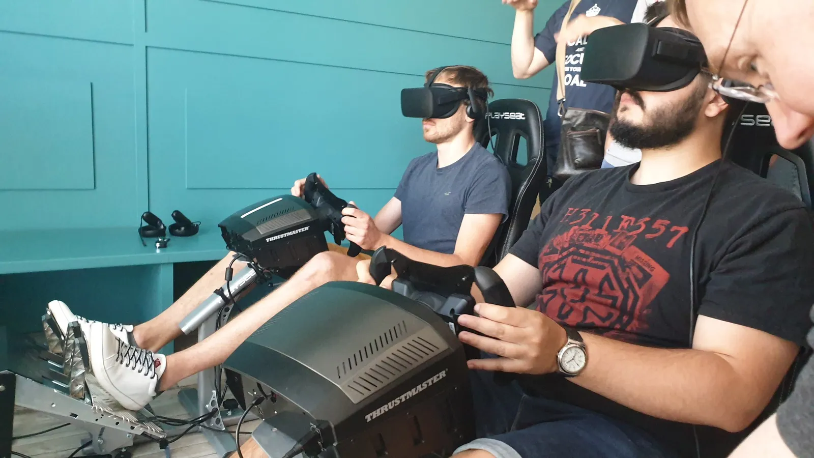 Deux participants casqués dans des sièges de simulation de course, volant et pédalier en main