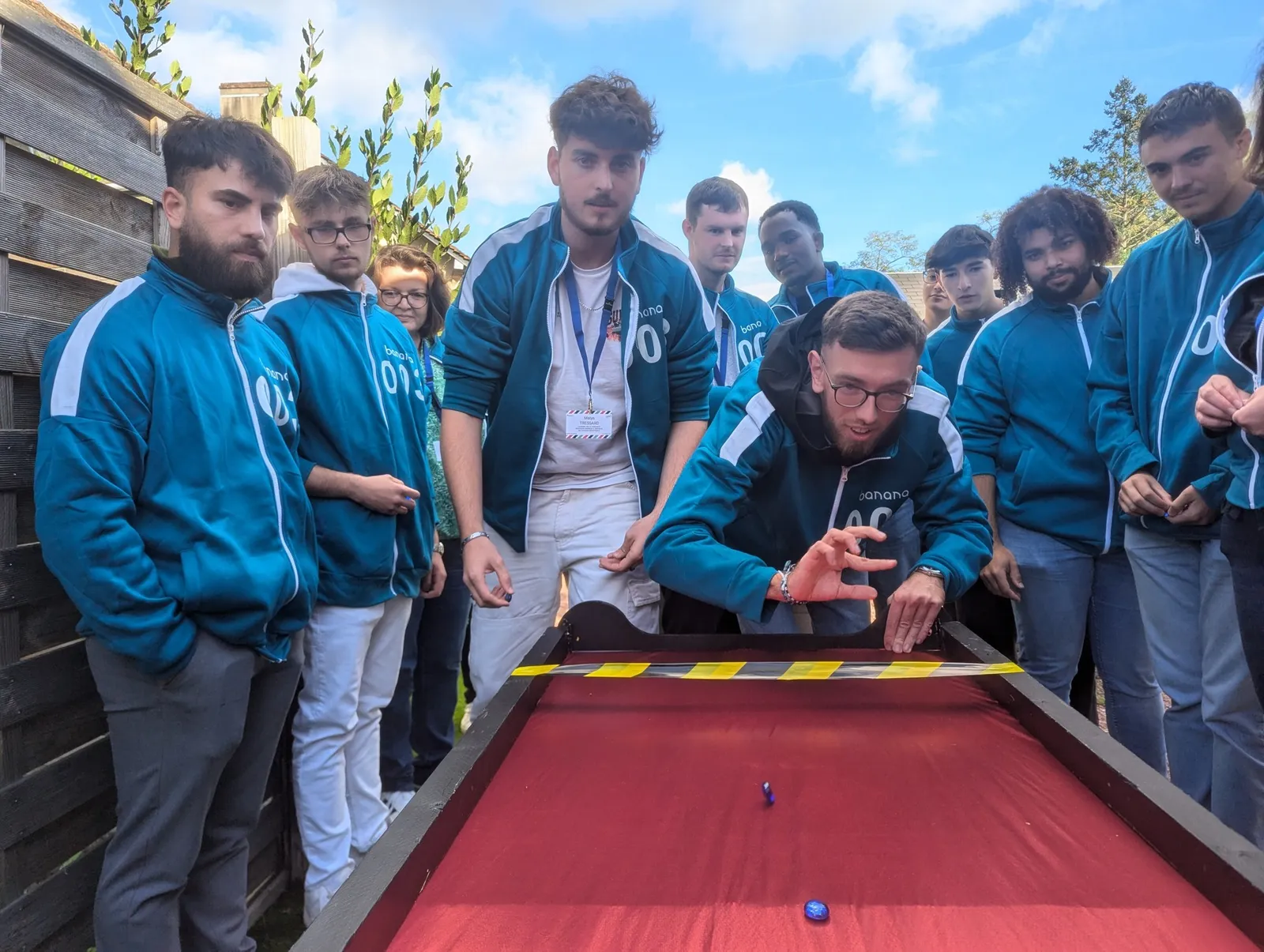 Équipe en survêtement bleu-vert numéroté qui regarde un jeu de billes sur une table rouge